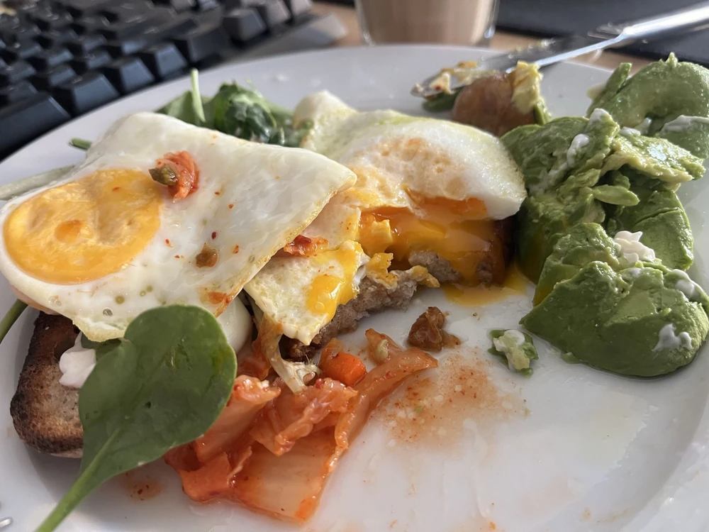 Eggs, kimchi and avocado on a plate, with a keyboard and coffee in the background.